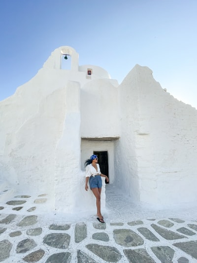 During the day, wearing blue denim shorts woman standing in the white cement wall
